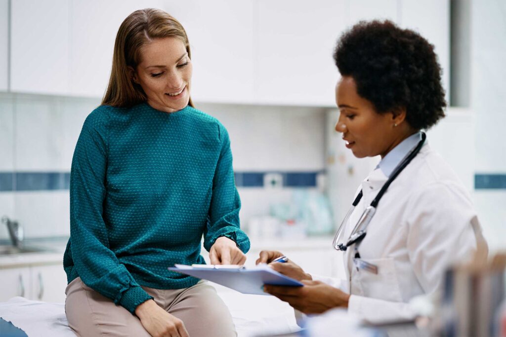 African American doctor and her female patient analyzing medical report after examination in the hospital. Focus is on female patient.