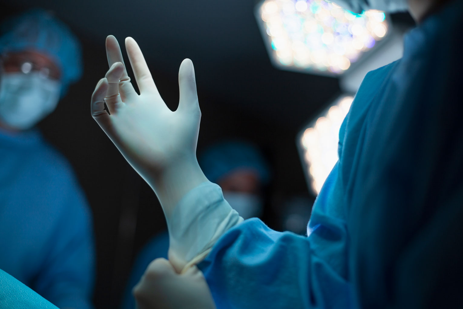 Medical professional doctor nurse preparing for surgery putting on wearing latex glove protective workwear on hand for safety in operation room in hospital with colleagues