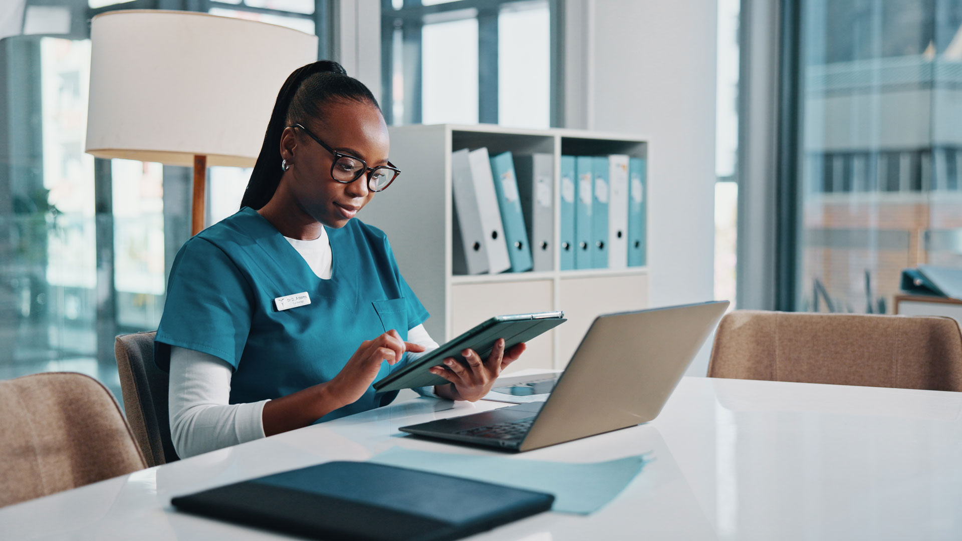 Black woman, doctor and typing with tablet at hospital for research, laboratory results and medical report. Person, online and reading email for Telehealth, schedule update and treatment information