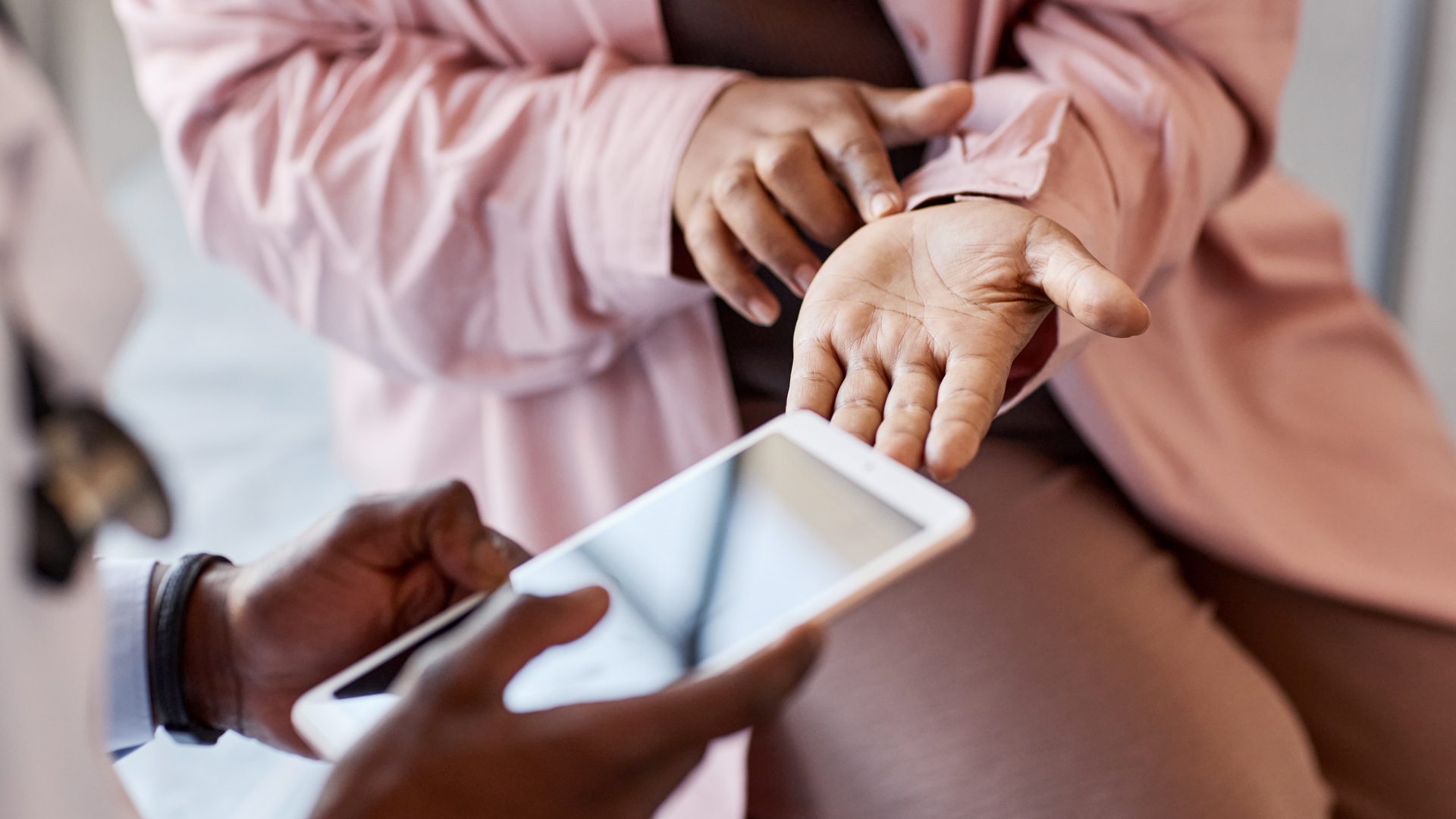 Close up of unrecognizable African American woman pointing at skin rash on hands while talking to doctor holding tablet in clinic copy space, qqfs, healthcare professionals with hand eczema